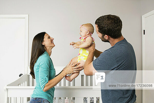 Mid adult couple holding up baby daughter in nursery