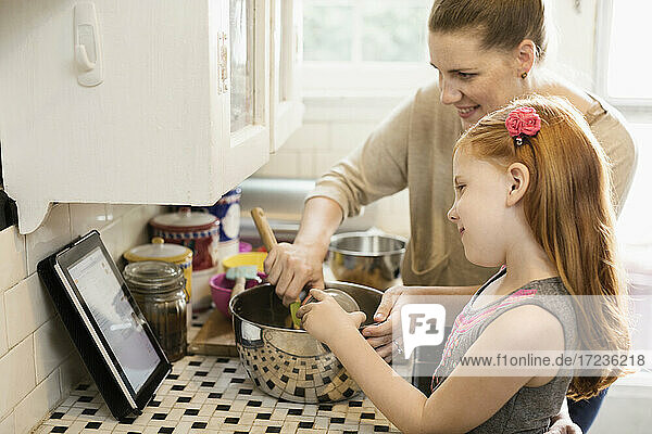 Mädchen und Mutter schauen auf Rezept auf digitalem Tablet in der Küche