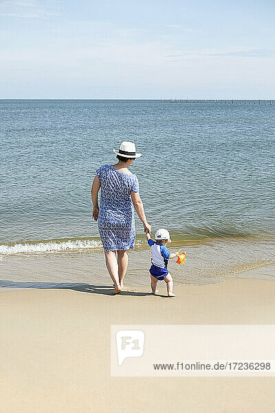 Mutter und junger Sohn  Hände haltend  am Strand spazierend  Rückansicht