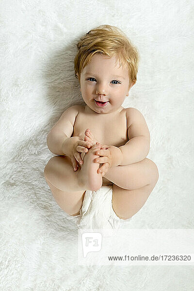 Kleinkind auf Decke liegend  Füße haltend  lächelnd