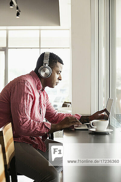 Junger Mann in einem Café  mit Kopfhörern  mit Laptop