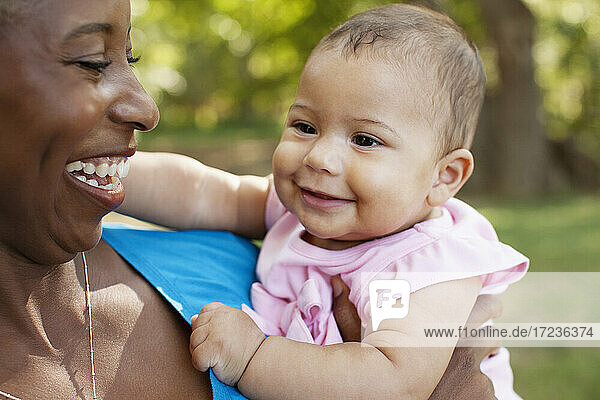 Head and shoulders of mother holding baby girl looking away smiling