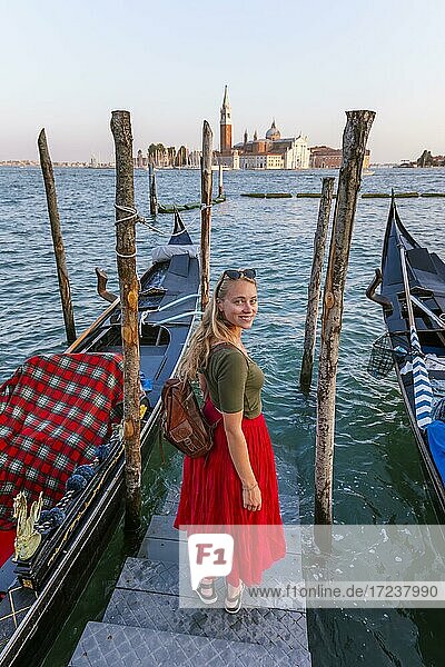 Young woman with red dress on a jetty  Venetian gondolas  in the back church San Giorgio Maggiore  Venice  Veneto  Italy  Europe