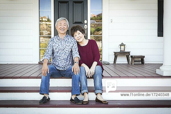 Attraktive glückliche ältere chinesische Paar sitzt auf den vorderen Stufen ihres Hauses