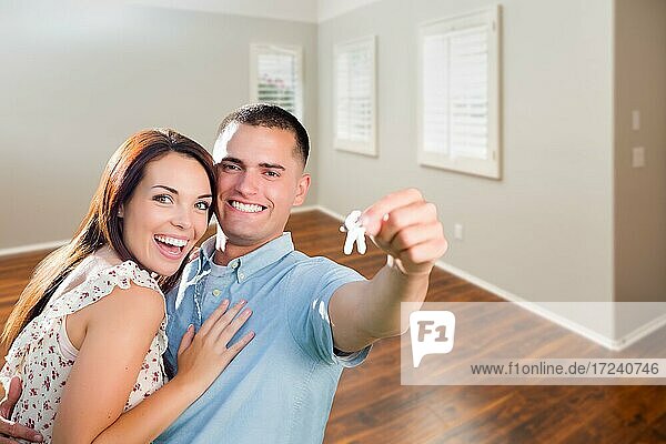 Junges Paar zeigt Hausschlüssel im leeren Zimmer des neuen Hauses