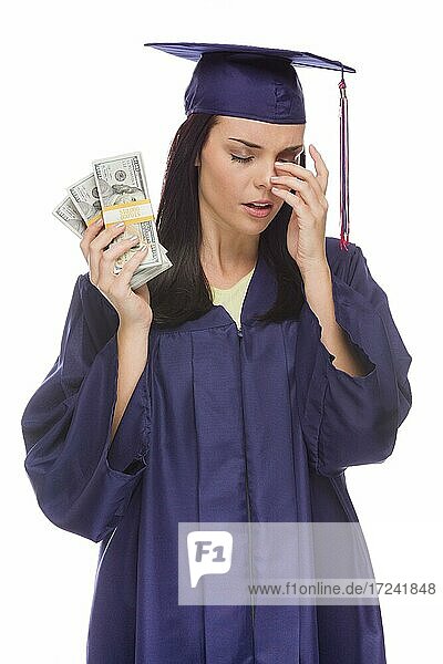 Gestresste weibliche Absolventin mit Kappe und Talar hält Stapel von Hundert-Dollar-Noten vor einem weißen Hintergrund