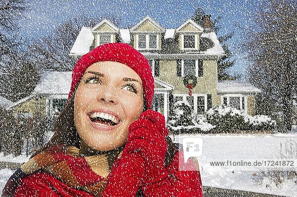 Lächelnde multiethnische Frau Blick zur Seite in Winterkleidung außerhalb von dekorierten Haus bei Schneefall