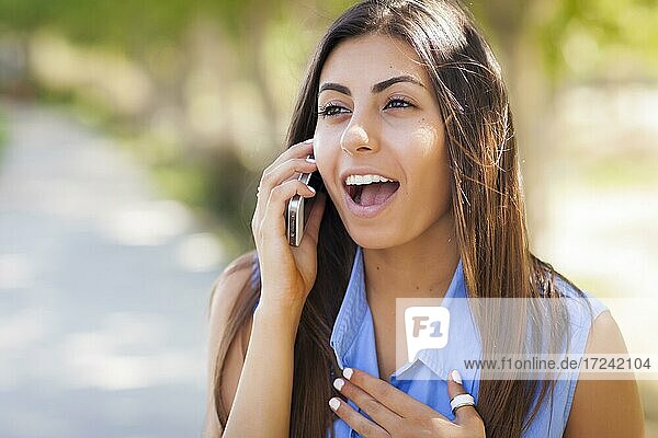 Lächelnde gemischtrassige junge erwachsene Frau  die ihr Mobiltelefon draußen benutzt