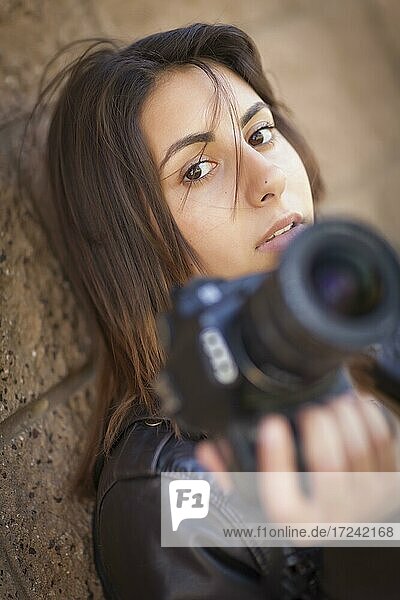 Attractive mixed-race young adult female photographer against wall holding camera