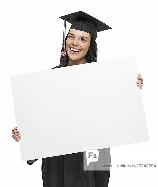 Glückliche gemischtrassige Absolventin mit Kappe und Talar hält leeres Schild vor weißem Hintergrund