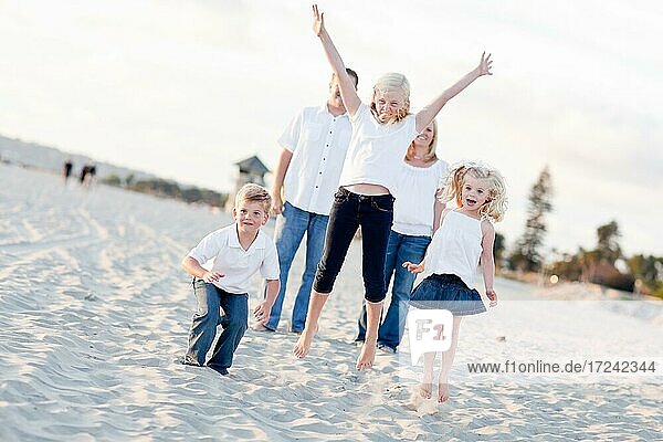 Happy sibling children jumping for joy at the beach as parents watch