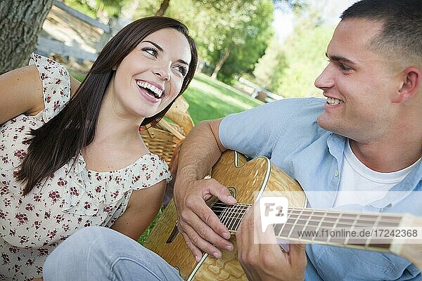 Happy mixed-race couple at the park playing guitar and singing songs
