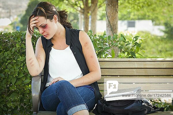 Sad bruised and battered young woman sitting on bench outside at a park