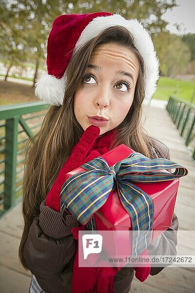 Hübsche festlich gekleidete lächelnde Frau trägt einen Weihnachtsmann Hut mit eingewickelten Geschenk außerhalb