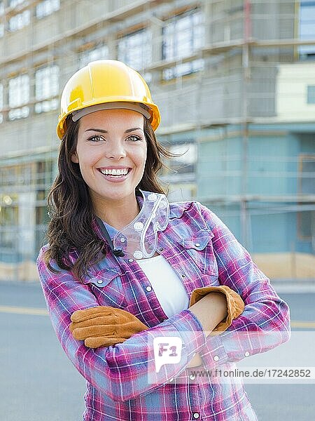 Porträt einer jungen attraktiven Bauarbeiterin mit Handschuhen  Schutzhelm und Schutzbrille auf einer Baustelle