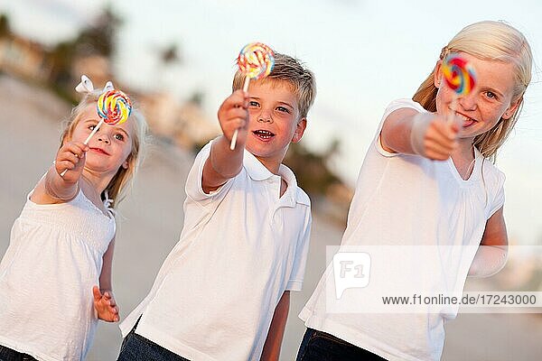 Cute brother and sisters enjoying their lollipops outside at the beach