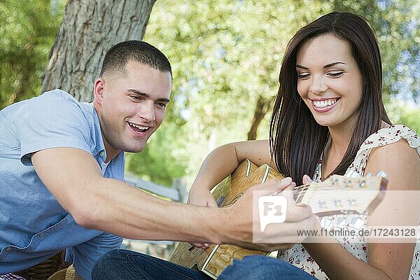Gutaussehender junger Mann bringt einem gemischtrassigen Mädchen im Park das Gitarrenspiel bei