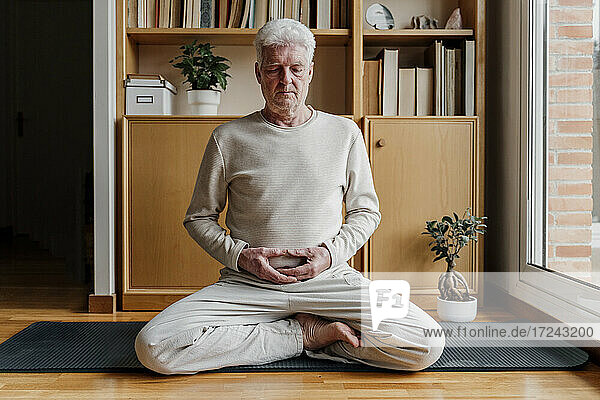 Senior man meditating while sitting with cross-legged at home