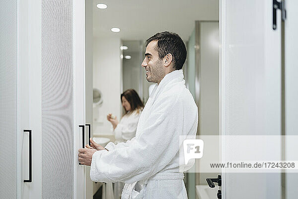 Smiling man in bathrobe opening cupboard in hotel
