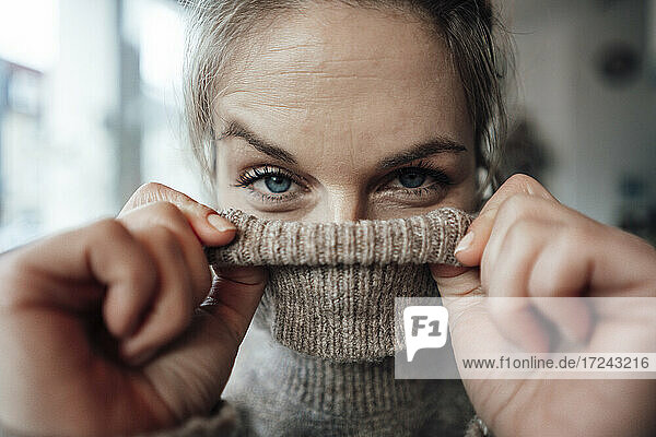 Playful woman covering face in sweater at cafe