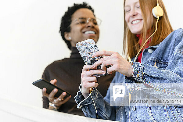 Cheerful woman with friend using smart phone