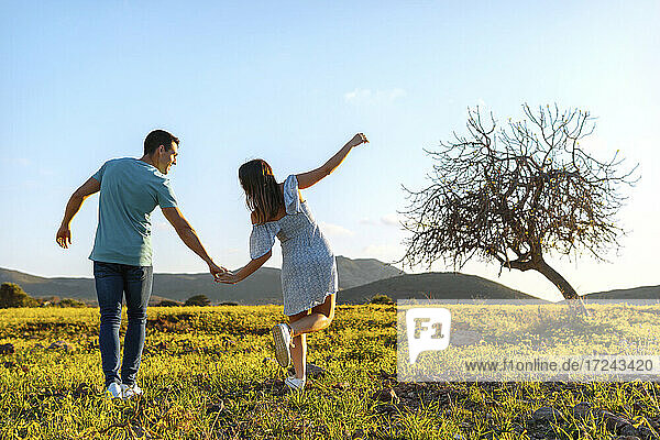 Junger Mann hält die Hand einer verspielten Frau im Gras
