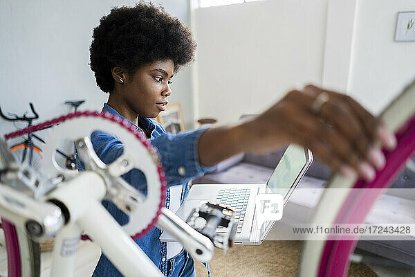 Afro hairstyle woman watching tutorial on laptop while repairing bicycle at home