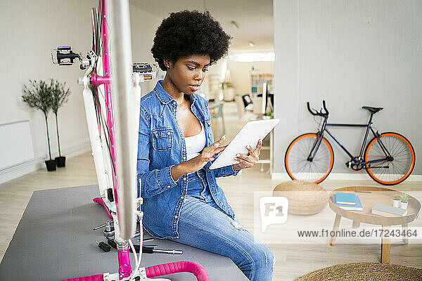 Afro-Frau sieht sich eine Anleitung auf einem digitalen Tablet an  während sie zu Hause ein Fahrrad repariert