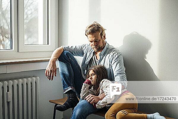 Girl resting on father's lap sitting at home
