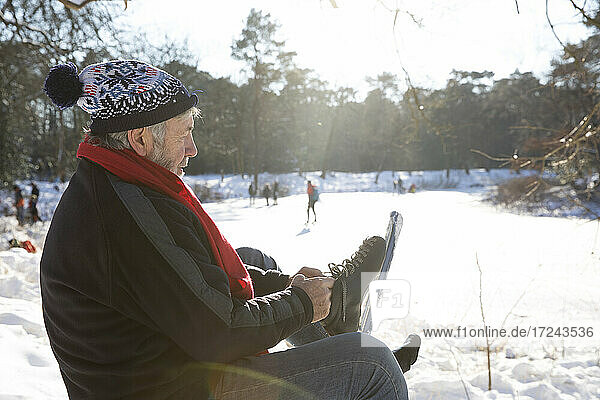 Senior man wearing ice skate while sitting on snow during winter