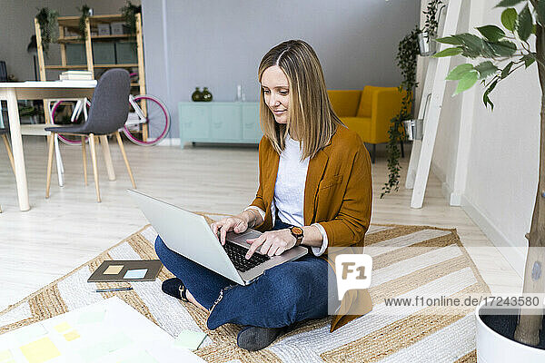 Weibliche kreative Geschäftsfrau mit Laptop auf Teppich im Büro