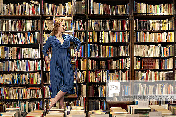 Lächelnde Frau schaut weg  während sie auf einer Leiter in einer Bibliothek steht