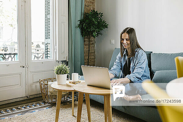 Geschäftsfrau lächelt  während sie während einer Videokonferenz im Büro zu Hause auf ihren Laptop schaut