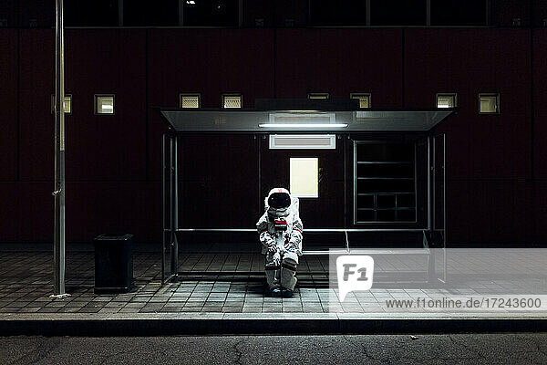 Astronautin sitzt nachts an der Bushaltestelle