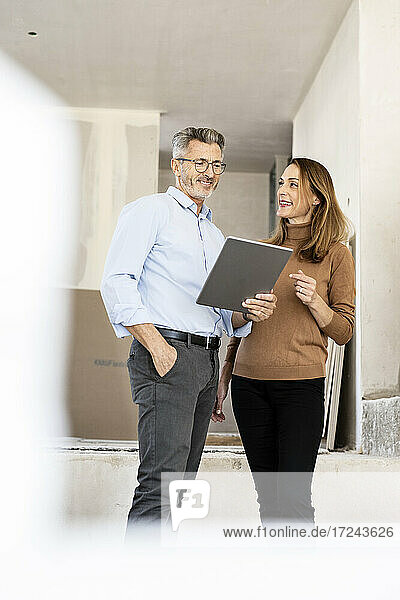 Smiling female colleague looking at male architect holding digital tablet at construction site