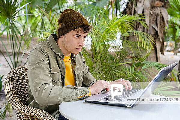 Junger Mann mit Laptop auf einem Tisch in einem Straßencafé
