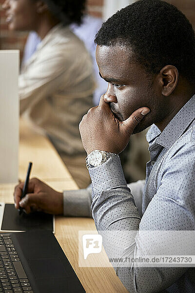Thoughtful male design professional using graphic tablet at coworking office