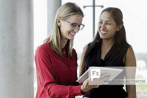 Lächelnde Geschäftsfrau  die ein digitales Tablet von einer Kollegin im Büro benutzt