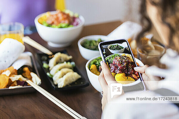 Frau fotografiert Essen mit dem Handy im Restaurant