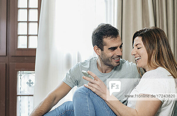 Lächelnder Mann  der eine Frau ansieht  die im Hotelzimmer ein Mobiltelefon benutzt