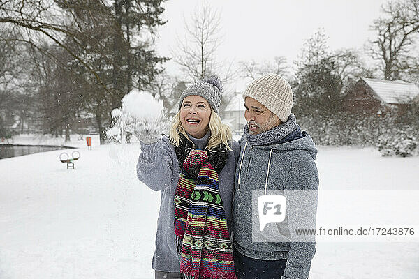 Cheerful woman throwing snow while standing with man at park