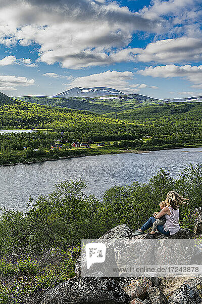 Mutter und kleiner Sohn bewundern die Aussicht auf den Fluss Karasjohka  während sie auf einem Felsen sitzen