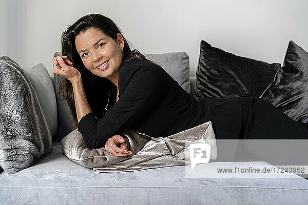 Lächelnde Frau  die sich zu Hause auf dem Sofa mit einem Kissen ausruht