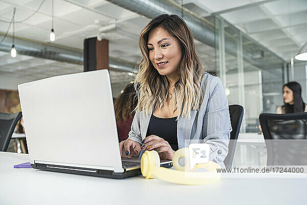 Lächelnde Unternehmerin mit Laptop am Schreibtisch in einem Coworking-Büro