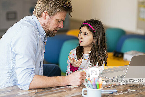 Mädchen gestikuliert beim Gespräch mit dem Vater während des E-Learnings am Tisch