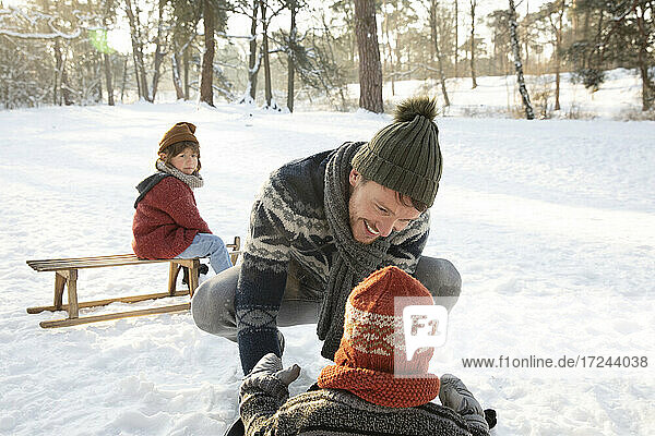 Smiling father in warm clothing playing with son on snow during winter