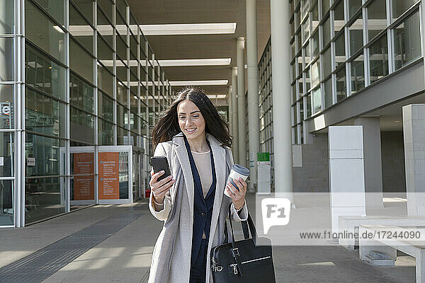 Junge Unternehmerin  die ein Mobiltelefon benutzt  während sie auf dem Gehweg steht