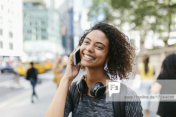 Glückliche Frau  die wegschaut  während sie mit einem Smartphone in der Stadt telefoniert