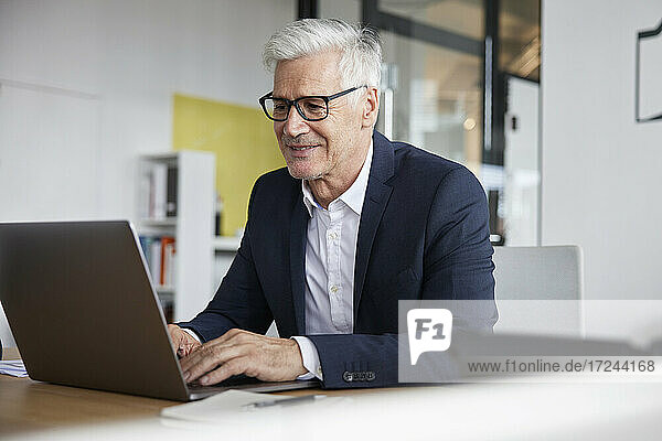 Smiling entrepreneur using laptop while working in office