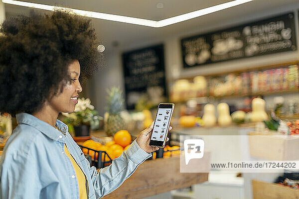 Afro-Frau  die eine mobile Anwendung in einem Lebensmittelgeschäft nutzt
